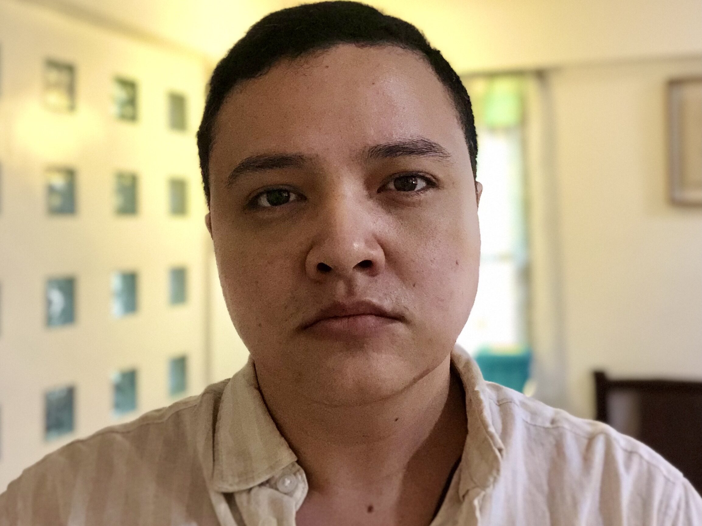 Nico from the collarbones-up. He's wearing a white, linen button-up shirt with the collar undone.